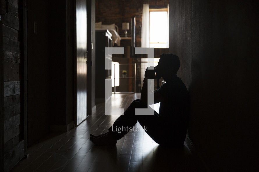 a man sitting in a dark hallway praying.