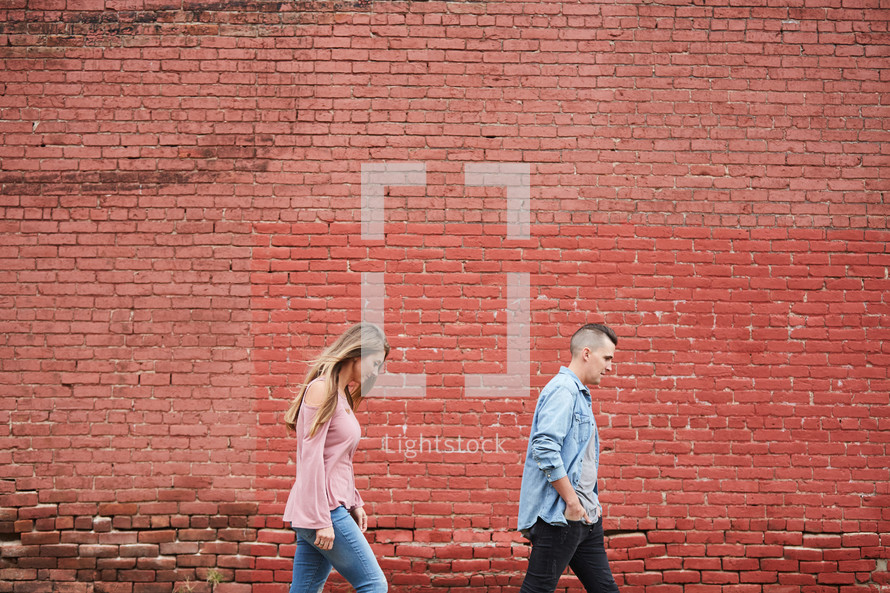 a couple walking in front of a red brick wall 