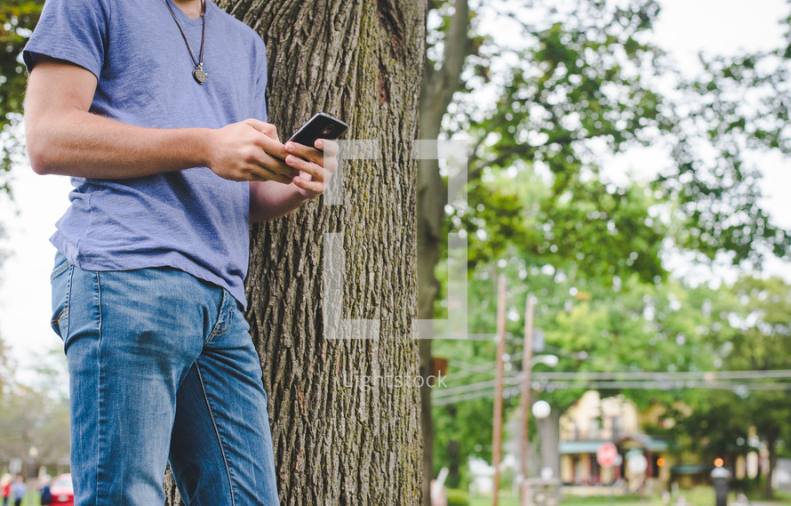man texting standing next to a tree 