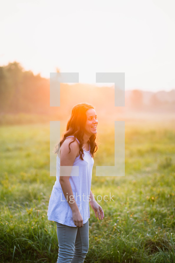 a woman standing alone in a meadow at sunrise 