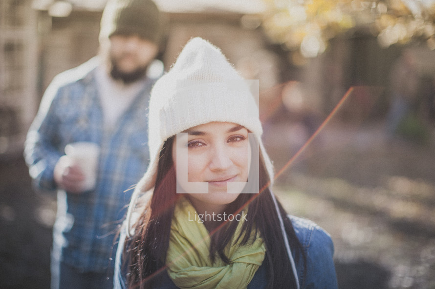 A woman smiling in the sunlight wearing a  white beanie