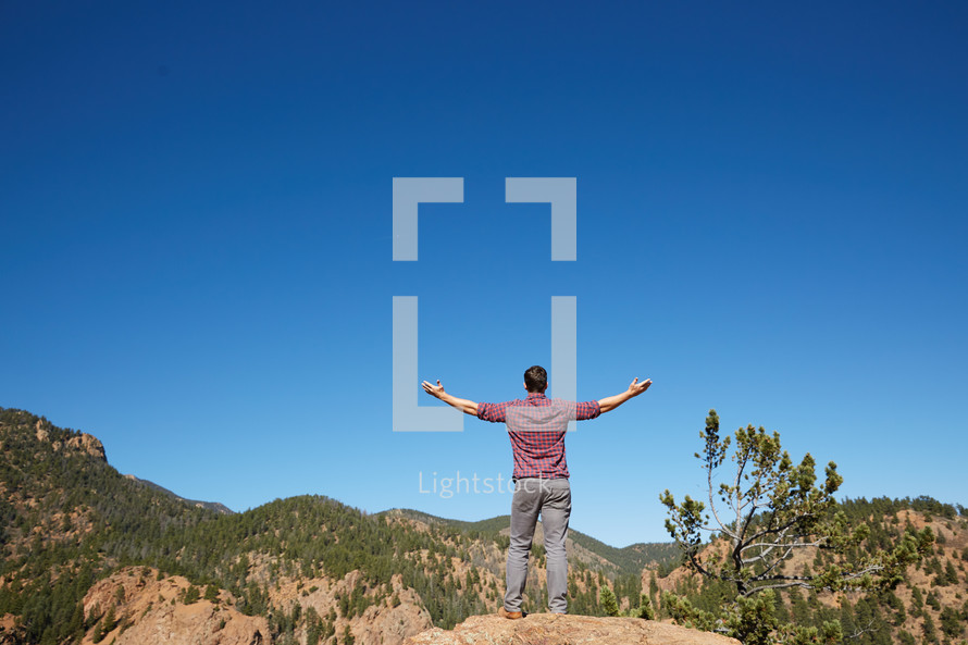 a man standing with open arms with mountain view 