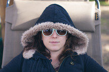 a woman in a hooded coat lying in a lounge chair 