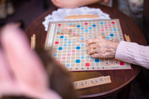 Elderly hands playing Scrabble on a wood table.