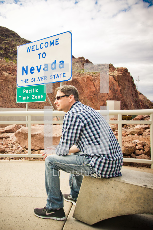 man sitting in front of a Welcome to Nevada sign