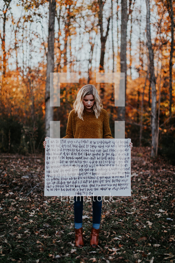 portrait of a woman standing outdoors holding a Bible verse sign 