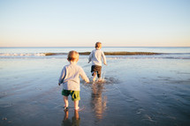 toddler boys running in tide on a beach 
