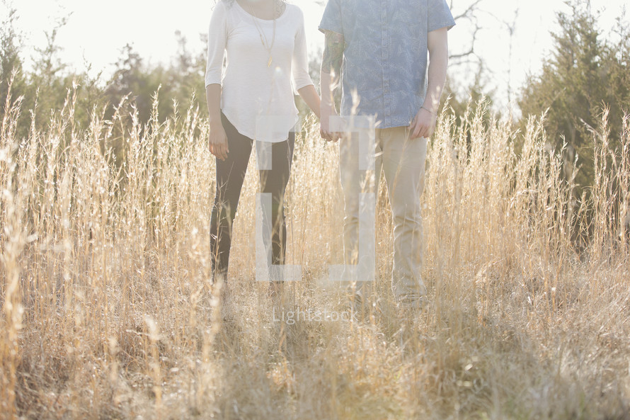 a couple holding hands outdoors in tall grasses