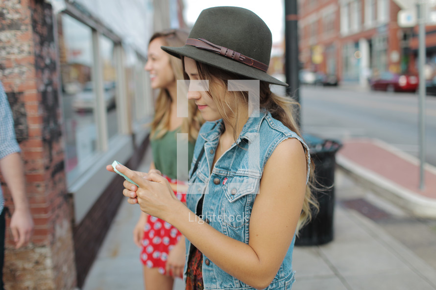 a young woman texting standing on a sidewalk with friends texting 