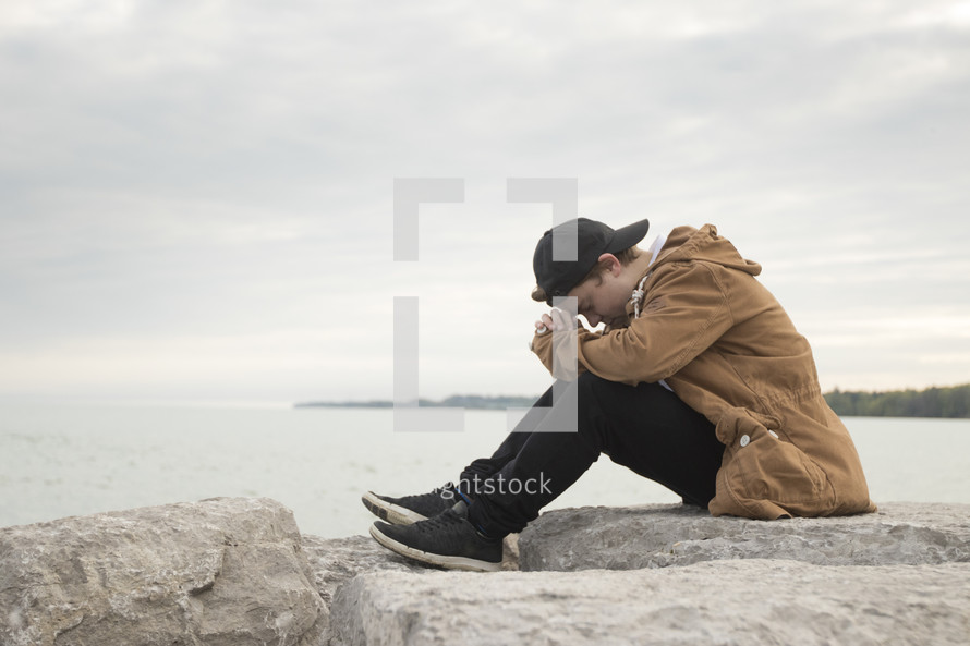 a man praying on a rock beside a quiet lake