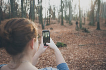 a woman taking a picture of a forest with her cellphone 