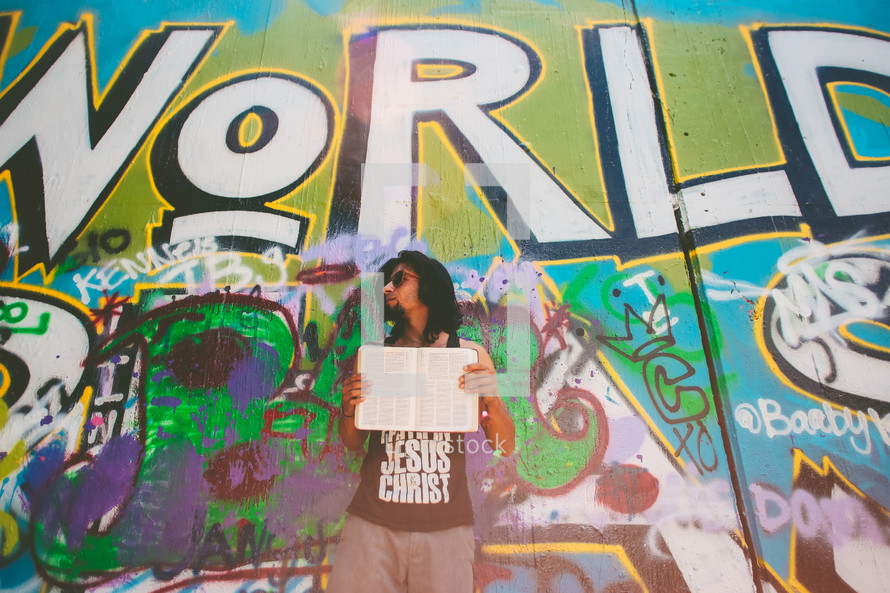 man standing in front of a graffiti covered wall holding a Bible 