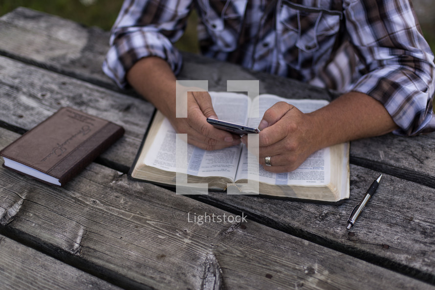 a man reading a Bible at a picnic table outdoors 