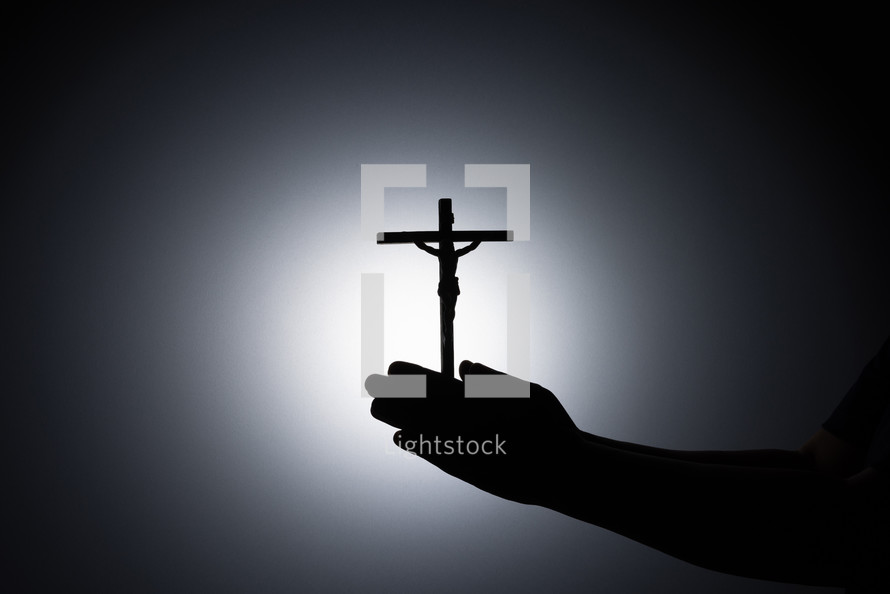 Silhouette photo - praying hands holding a crucifix