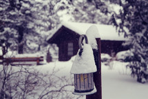 snow on a cabin and lantern 