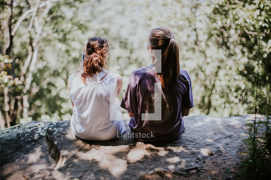 friends sitting together on a rock outdoors talking 
