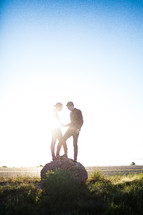 Sun glare on a couple standing together on a round boulder.