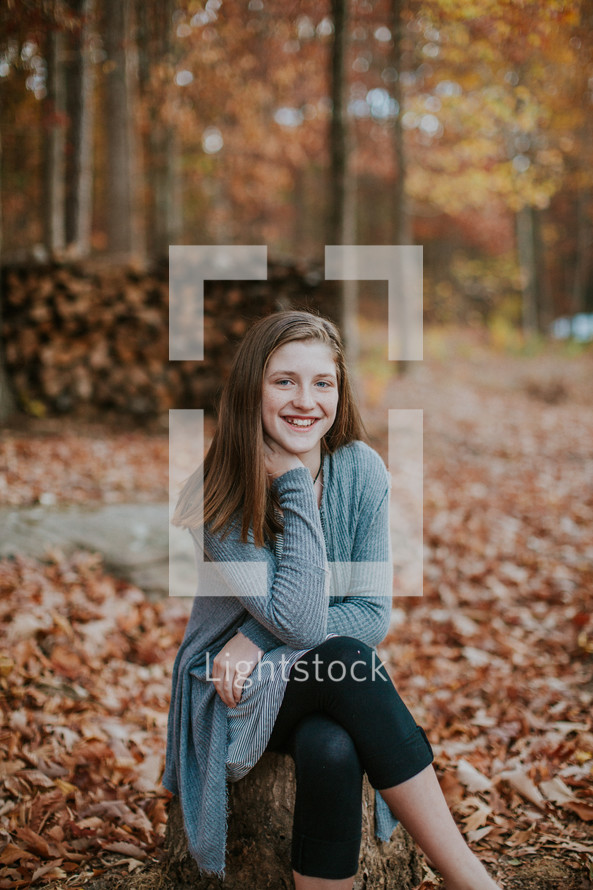 teen girl sitting on a tree stump outdoors in fall 