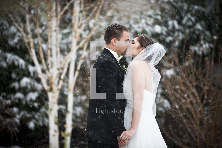 bride and groom kissing under falling snow
