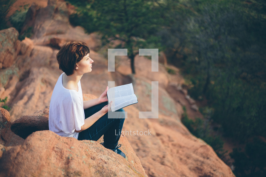 Woman sitting outside on a hilltop reading the Bible.