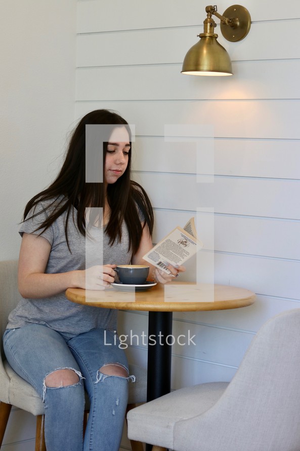a woman reading a book over a cup of coffee 