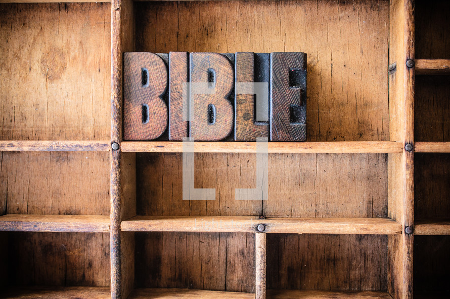 Wooden letter spelling "Bible" on a wooden bookshelf.