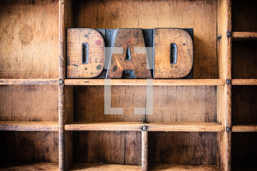 Wooden letters spelling "Dad" on a wooden bookshelf.