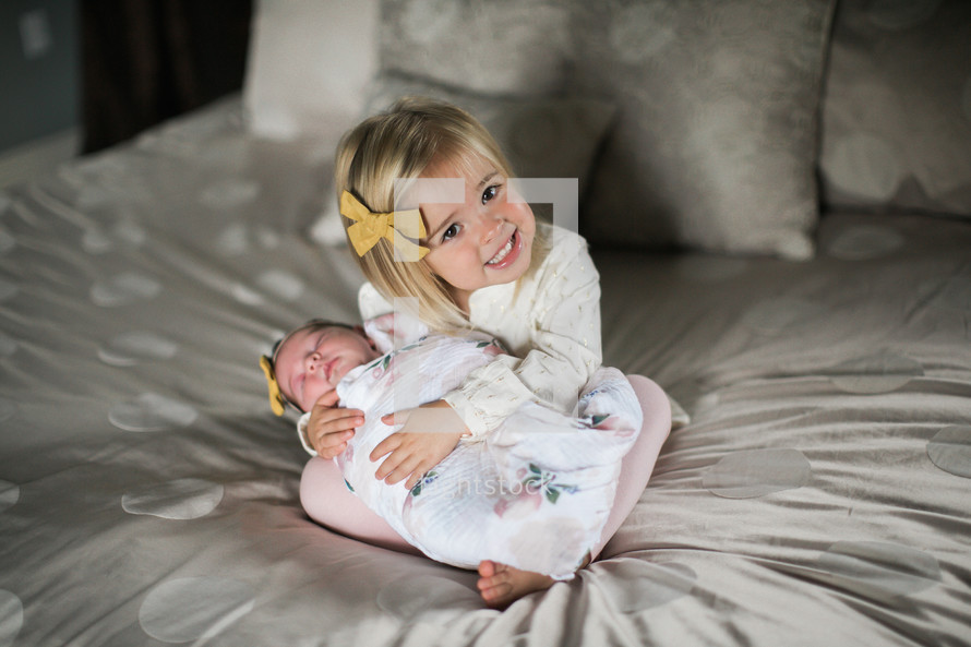 big sister holding her baby sister on a bed 