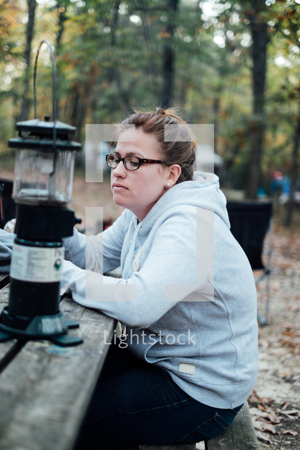 woman sitting at a picnic table at a campsite next to a lantern 
