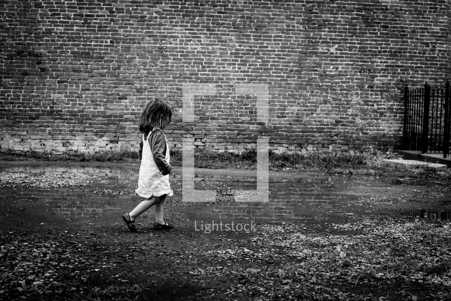 toddler girl walking in front of a brick wall 