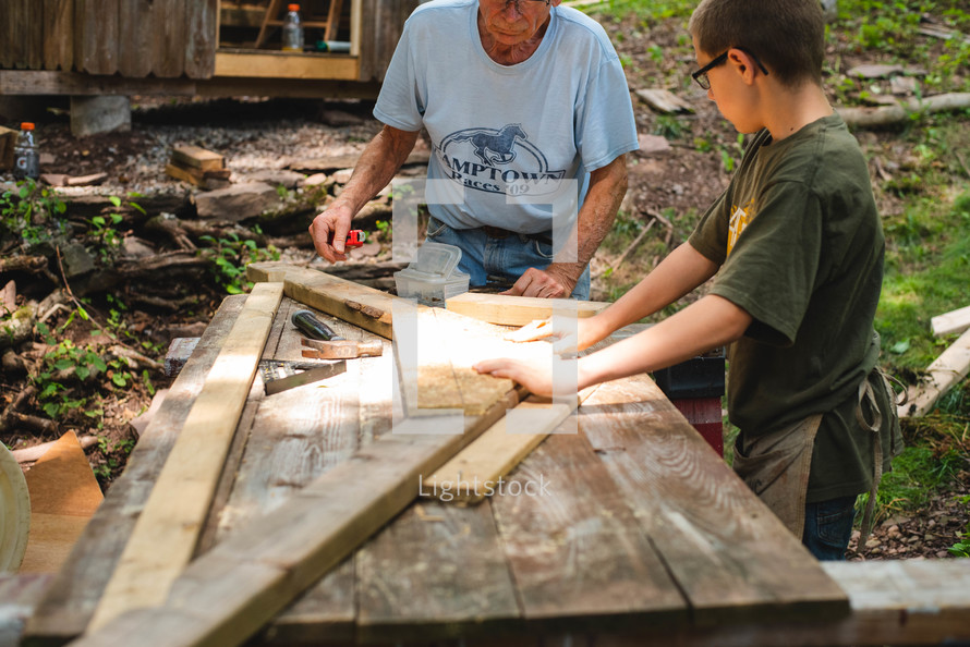 grandfather helping his grandson hammer nails into wood boards 
