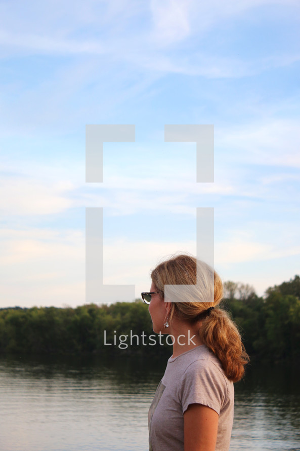  a woman with a ponytail looking out at lake water 