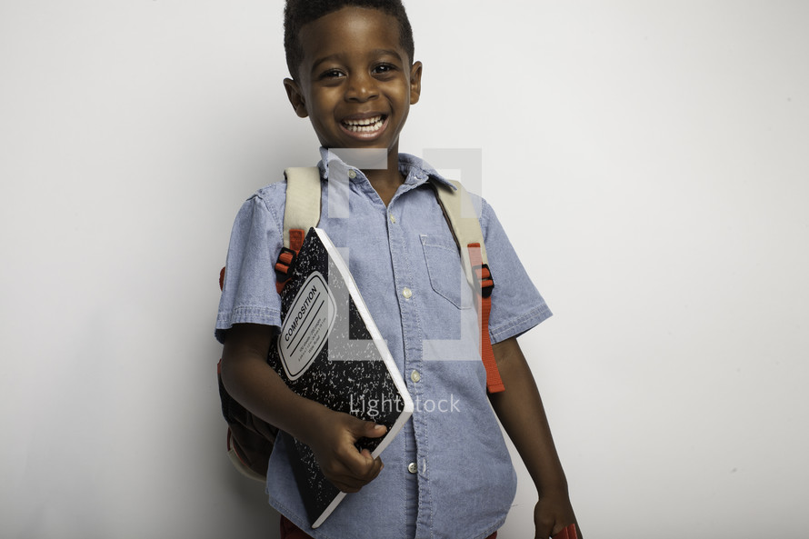 a boy with a book bag holding a composition notebook 