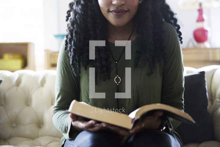 an African American woman reading a Bible on a couch 