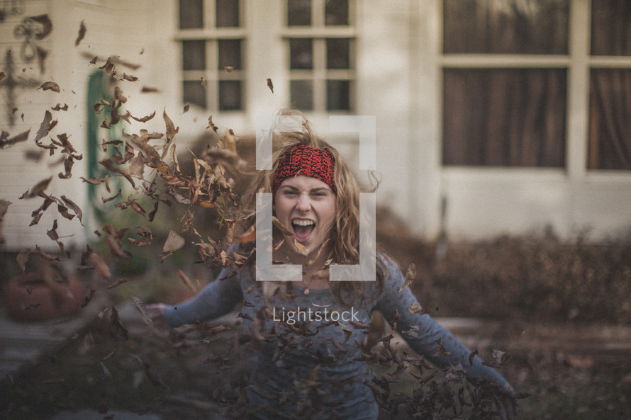 A blonde girl throwing fall leaves in the air