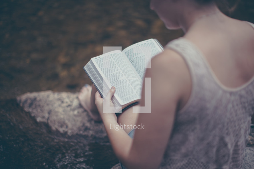 woman sitting on a rock reading a Bible