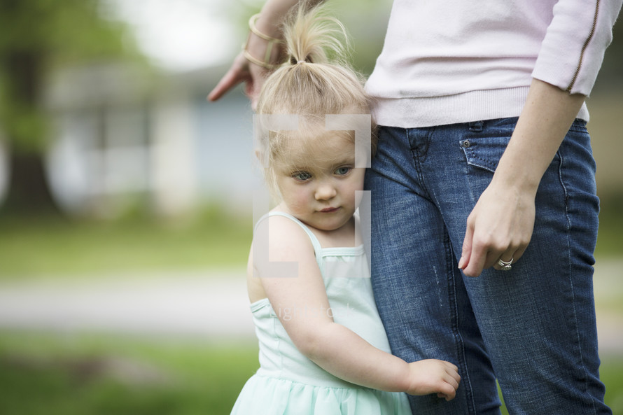 a toddler girl holding onto mother's leg 