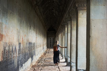 a woman walking under a covered stone corridor 