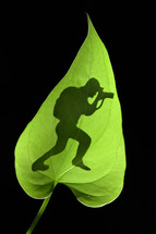 Photographer with camera silhouette behind of green leaf