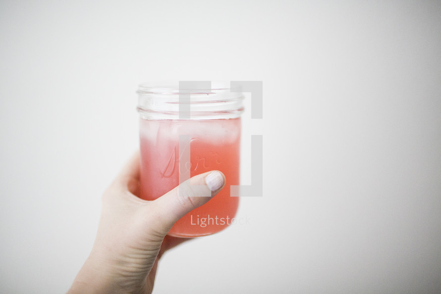 Woman's hand holding a glass filled with an iced beverage.