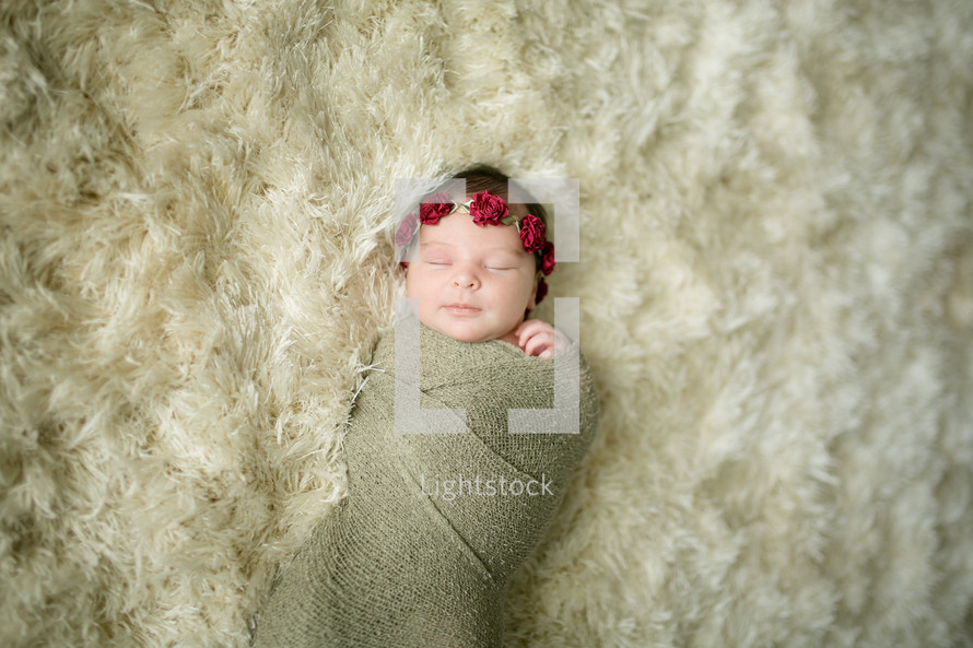 a swaddled newborn on a fur rug 