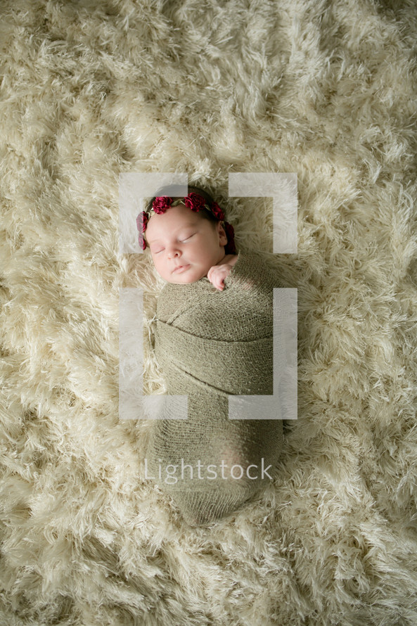 swaddled newborn on a fur rug 