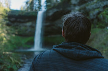 man looking up at a waterfall 