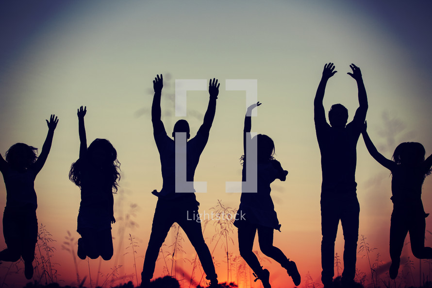 silhouettes of young adults jumping outdoors at sunset 