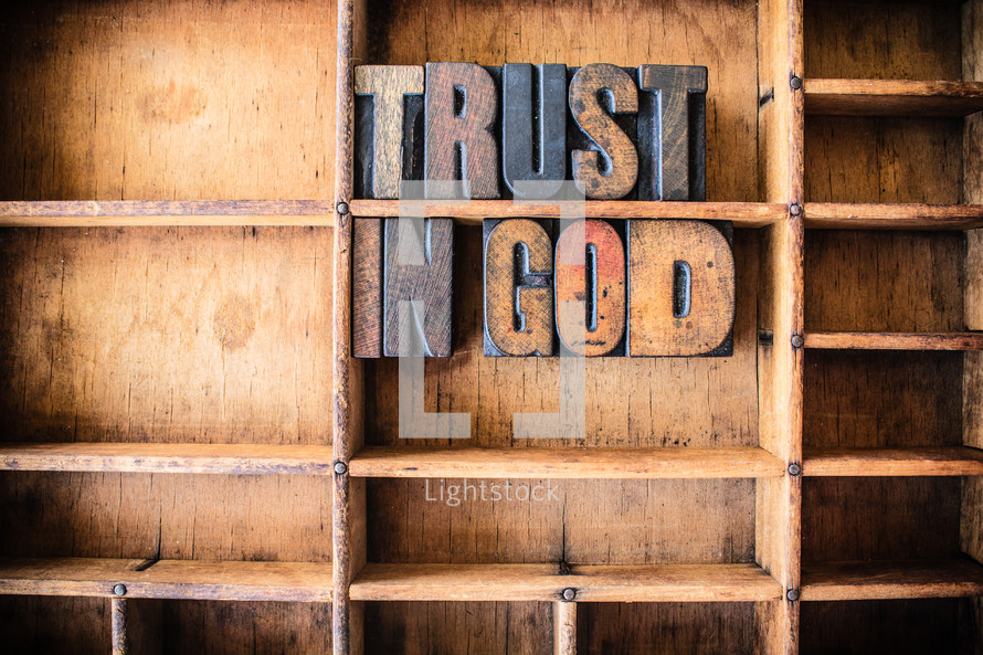 Wooden letters spelling "Trust in God" on a wooden bookshelf.