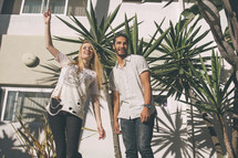 a man and a woman standing outdoors in front of tropical plants 
