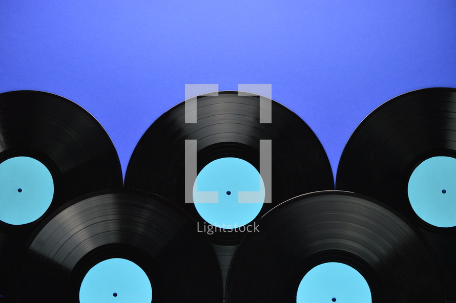 pile of old black vinyl records with blank cyan labels on blue background with copy space above