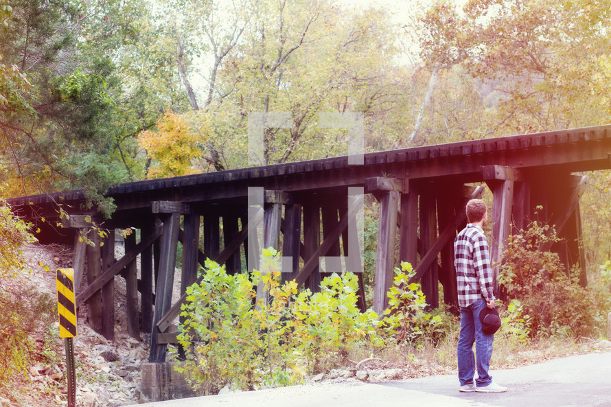 young man standing by a train bridge 