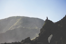 man sitting on a rock peak praising the Lord 