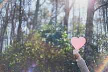 A woman holding a paper heart in the air outdoors 